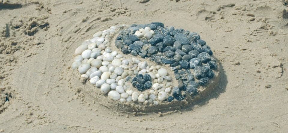 Een yin-yangteken van witte en grijze steentjes in het zand