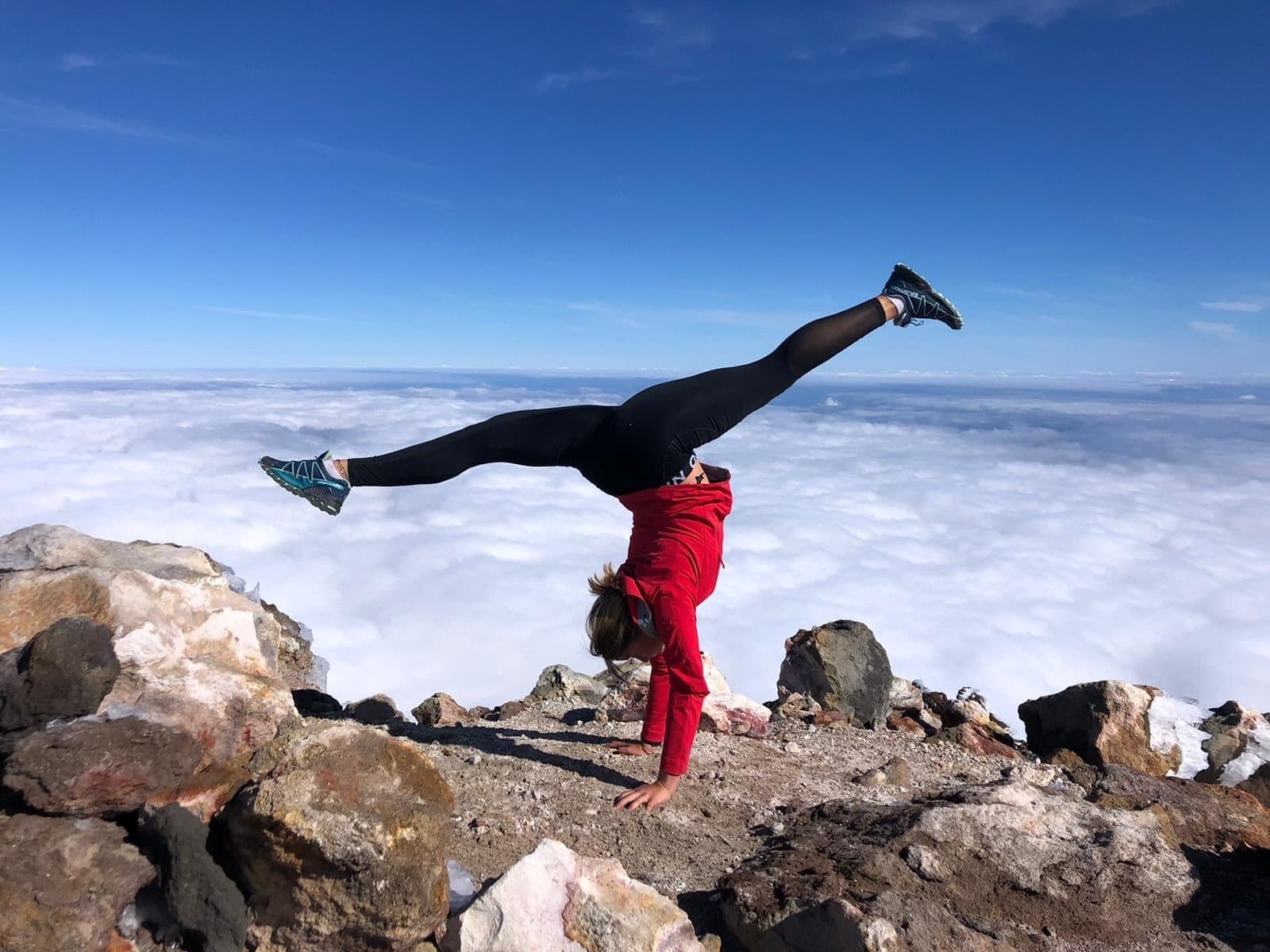 Een handstand in een rode jas op een bergtop boven de wolken