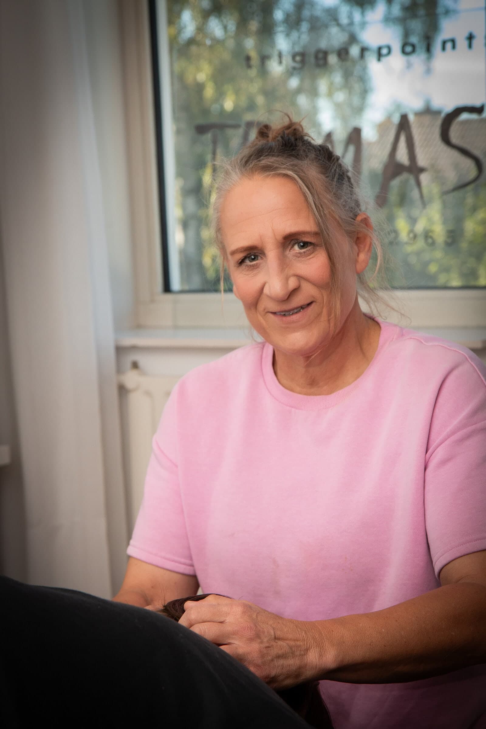 Hanneke Schuiling lachend in haar praktijk, met TRIMAS op het raam achter haar